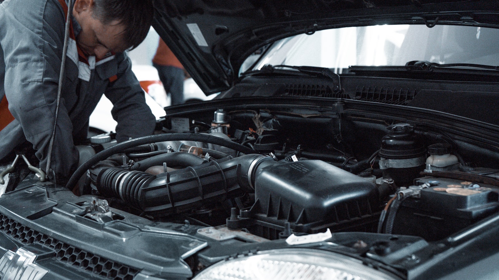 A mechanic leaning over an open hood, working on the engine